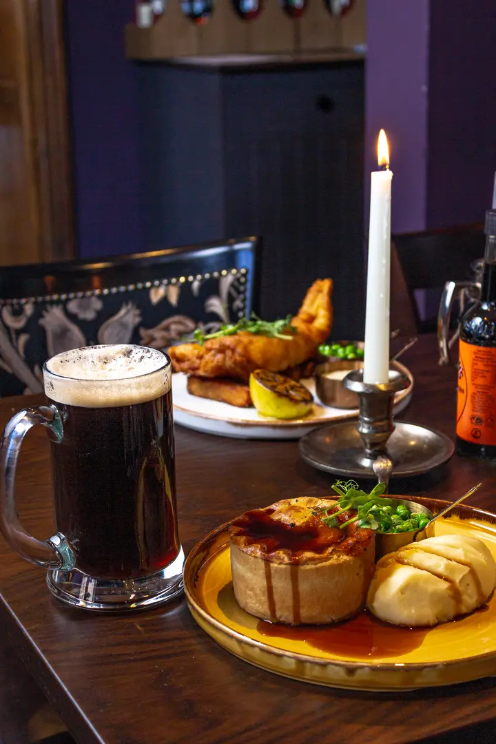 A pie with gravy and a tankard of stout on a dark table